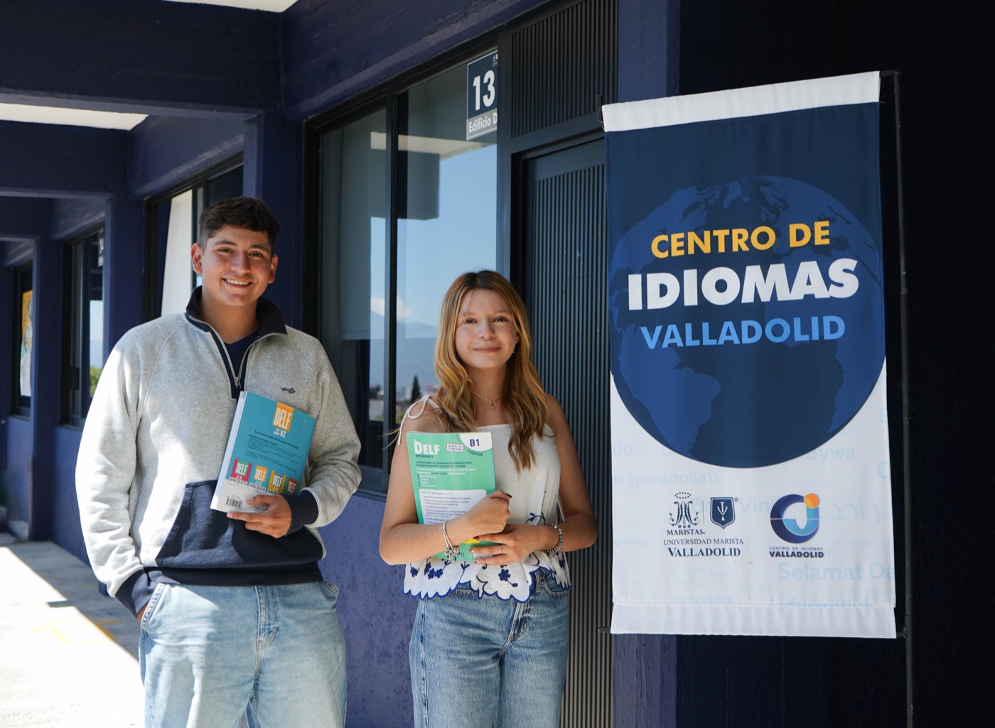 Dos estudiantes del Centro de Idiomas Valladolid junto al cartel del centro