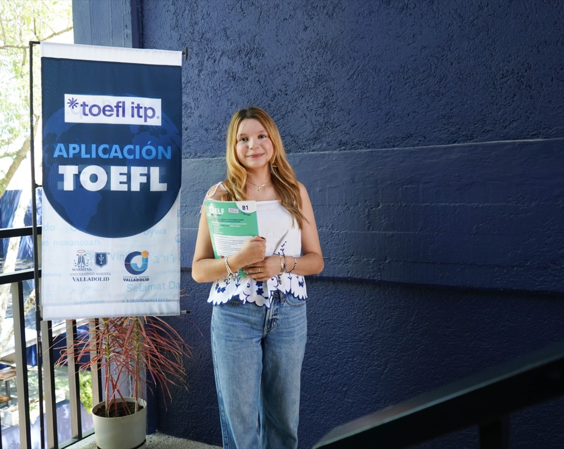 Una alumna del Centro de Idiomas Valladolid con su libro, junto al cartel de la aplicación TOEFL