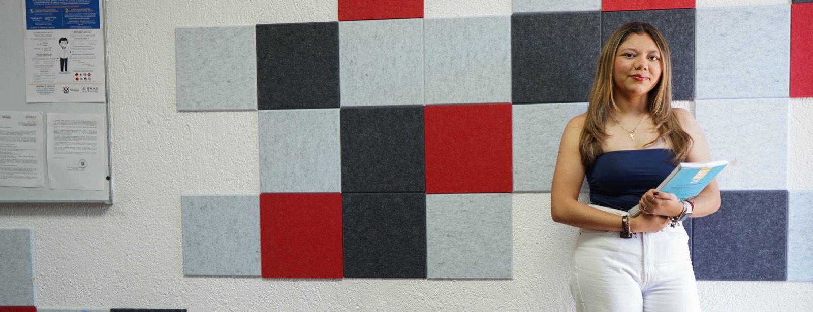 Una alumna del Centro de Idiomas Valladolid con su libro, delante del muro de paneles de las aulas